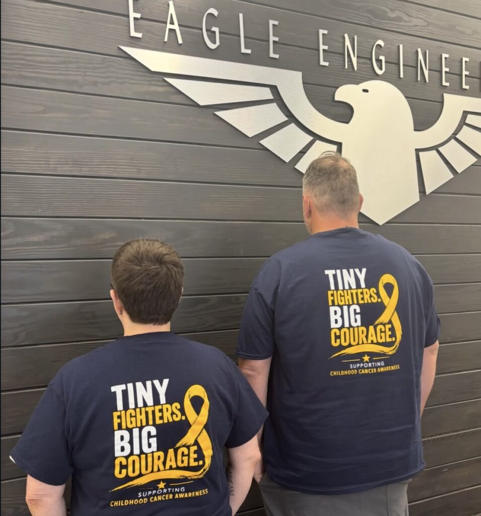 Eagle Engineering team members in Tiny Fighters Big Courage shirts in front of the Eagle Engineering sign