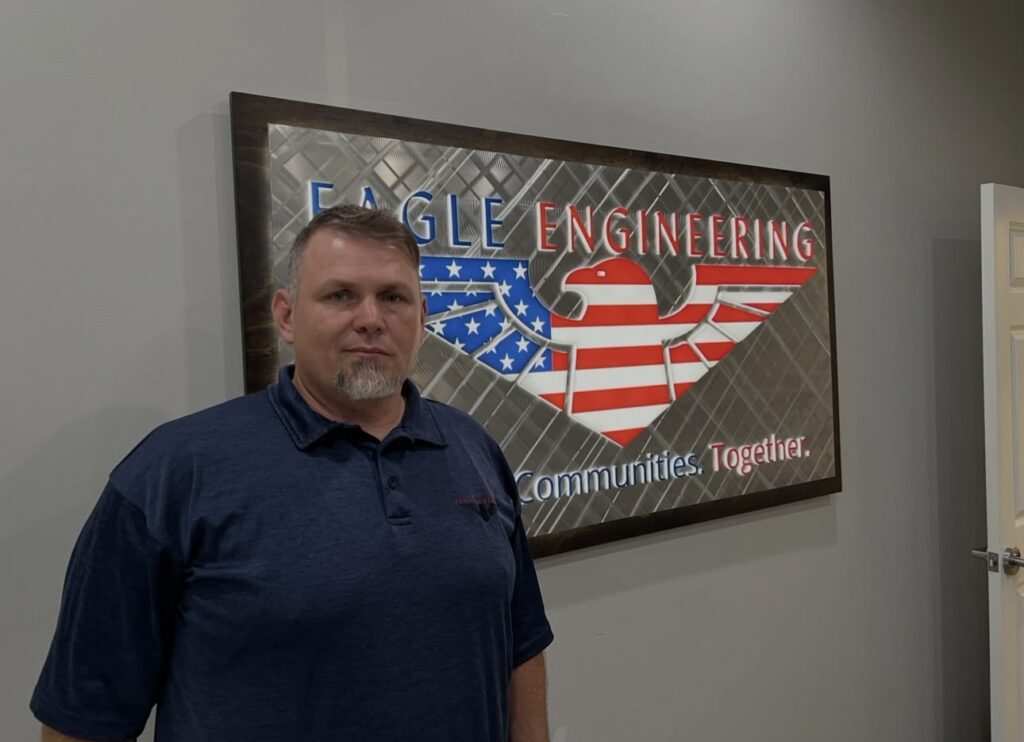 Eagle Engineering team member standing in front of the Eagle Engineering flag sign